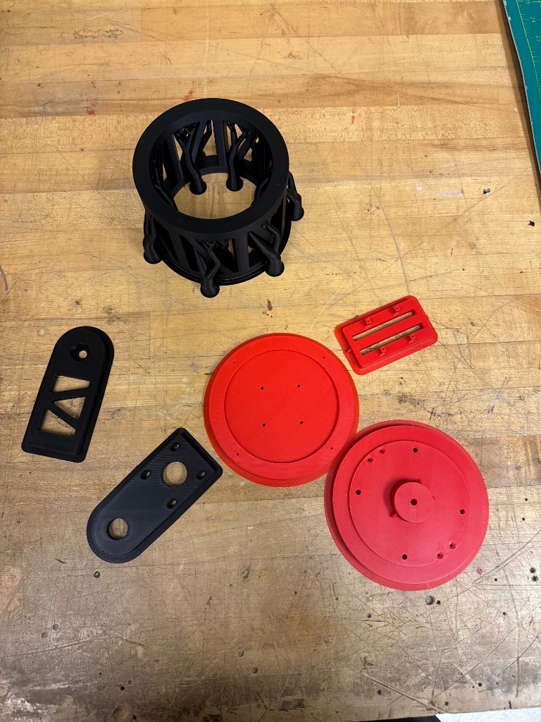 Black and red 3D-printed turret structural parts laid out on a workbench